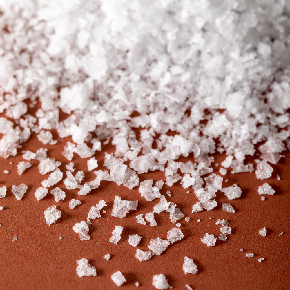 Detail of Jacobsen Pure Flake Sea Salt, on an orange tabletop.