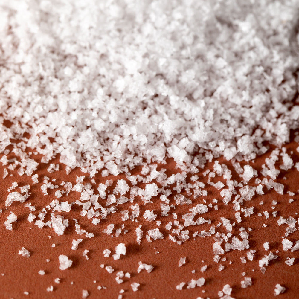 Detail of Jacobsen Pure Kosher Sea Salt, on an orange tabletop.