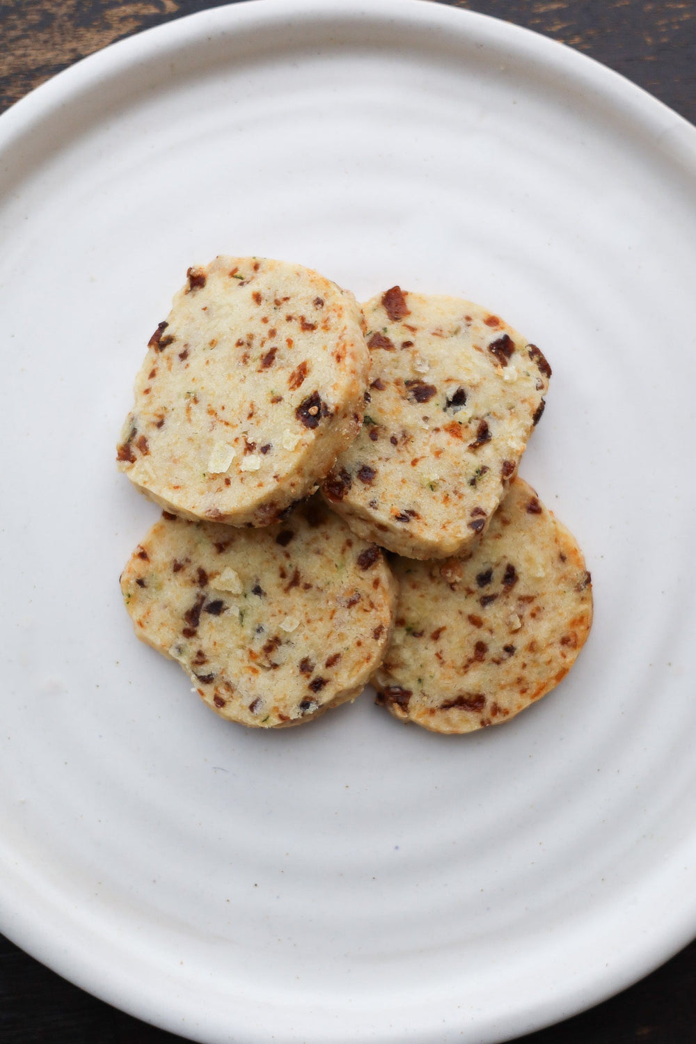 Four small tan colored shortbread cookies on a white plate.