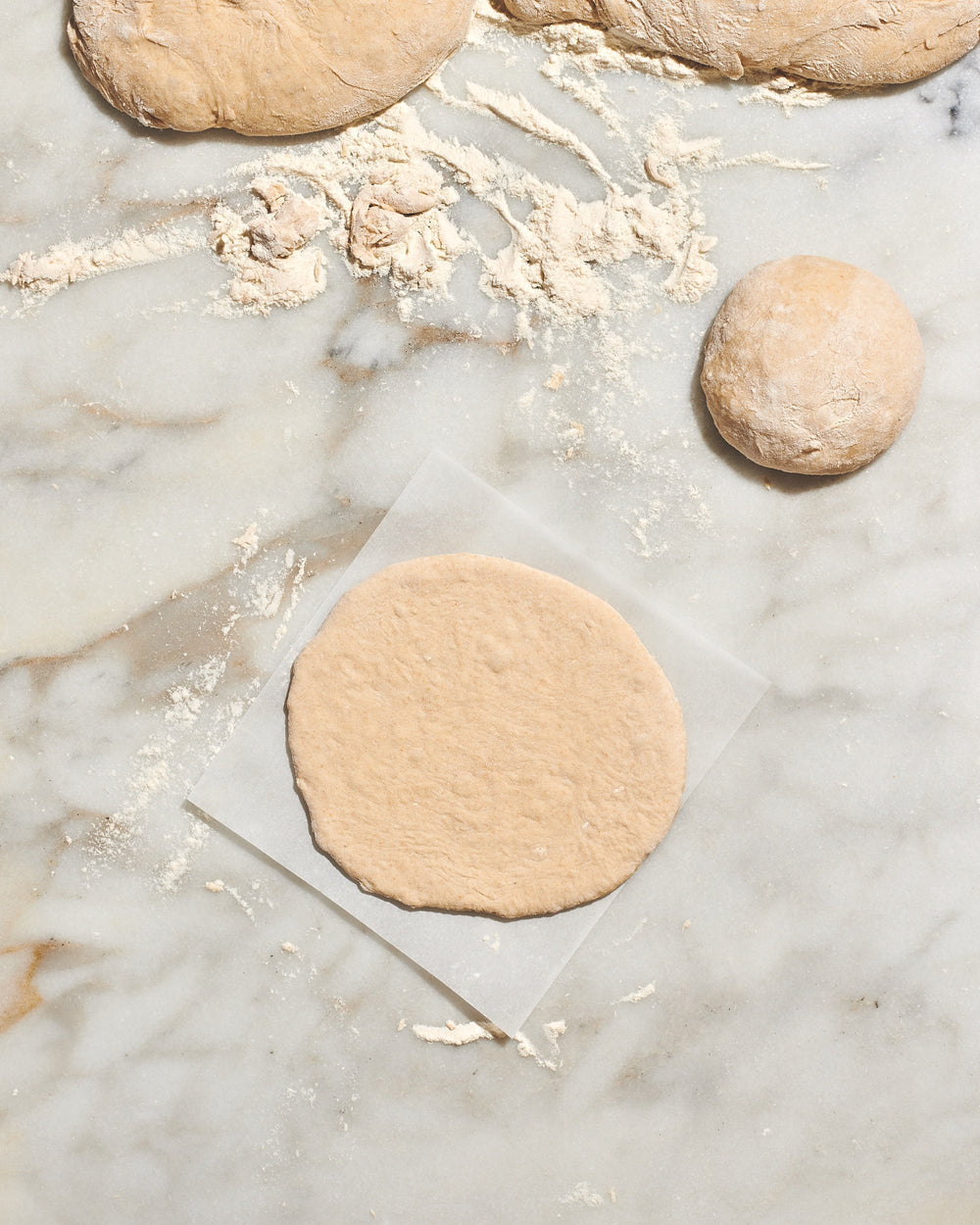 Pieces of raw pita dough and bits of flour on top of a granite countertop. 