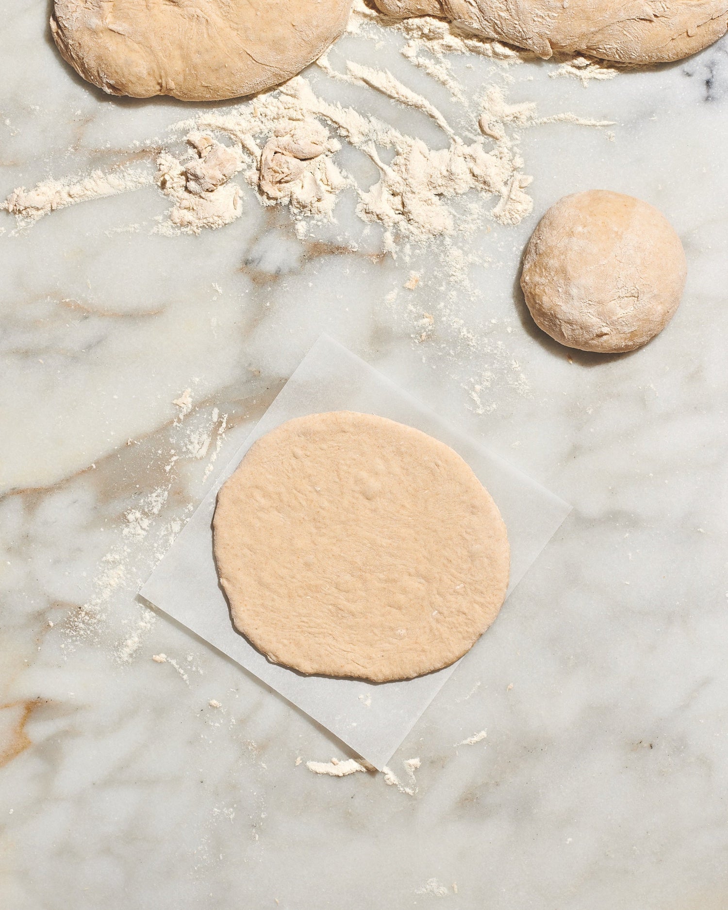Pieces of raw pita dough and bits of flour on top of a granite countertop. 