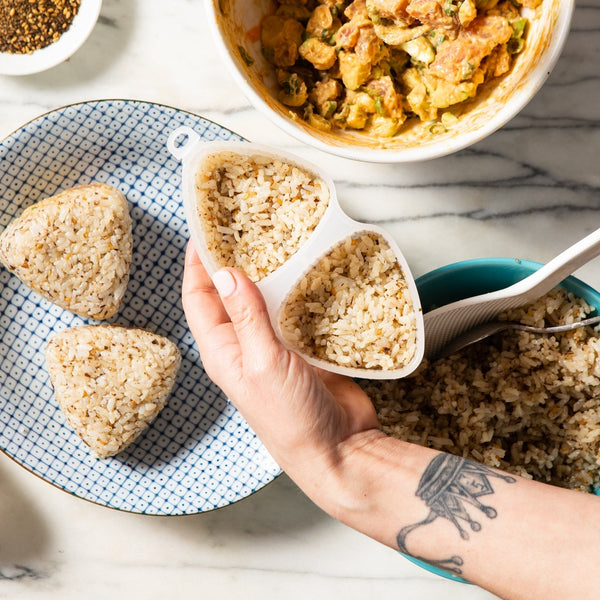 A person holds an onigiri mold, which is filled with rice.
