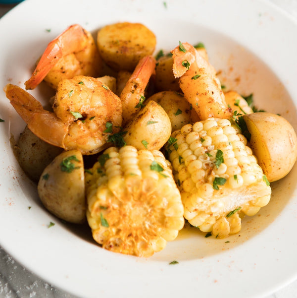 A sea food boil in a bowl with shrimp, corn, and potatoes.
