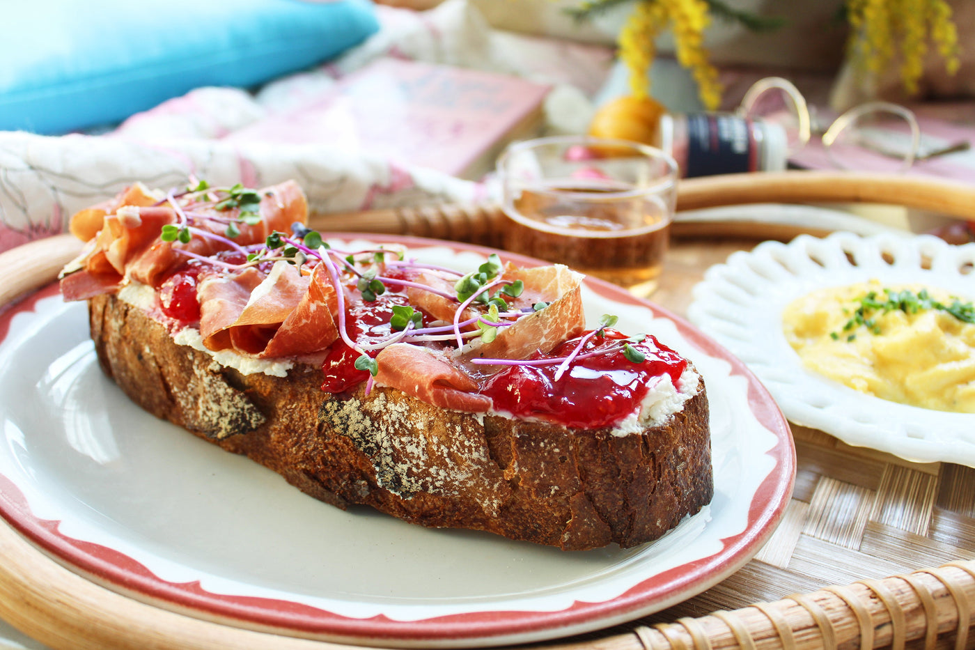 A slice of toast topped with raspberry jam, prosciutto and sprigs of micro greens.