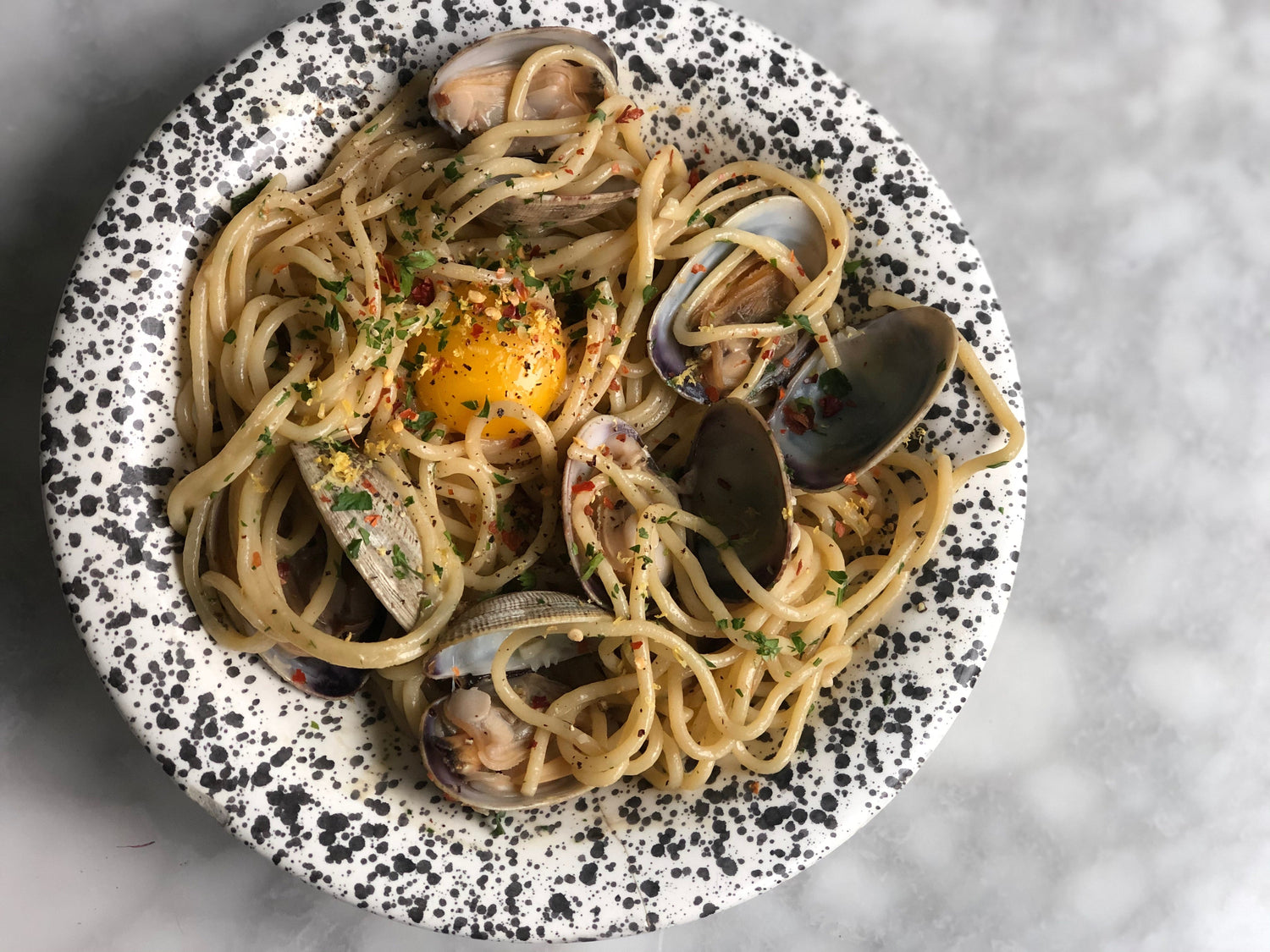 A plate with spaghetti noodles, clams, and an egg yolk.