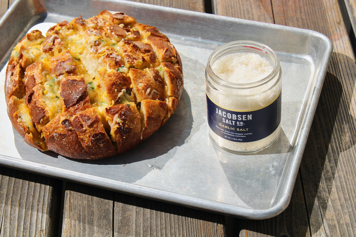 A sheet tray with cheesy bread and a jar of garlic salt.