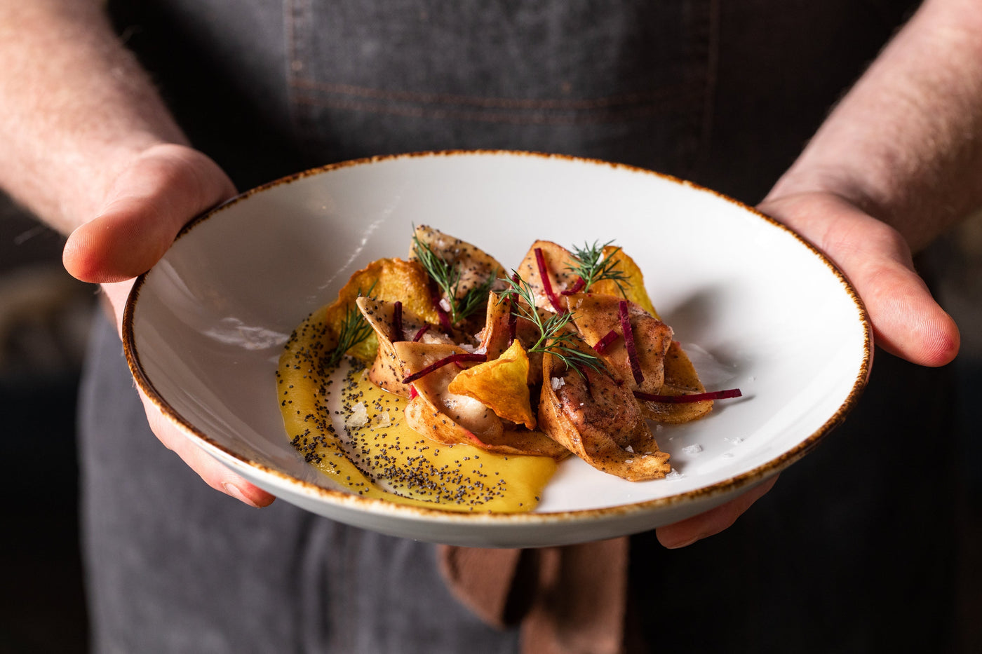 A close up of a chef's hands, presenting a plate of golden colored tortelli.