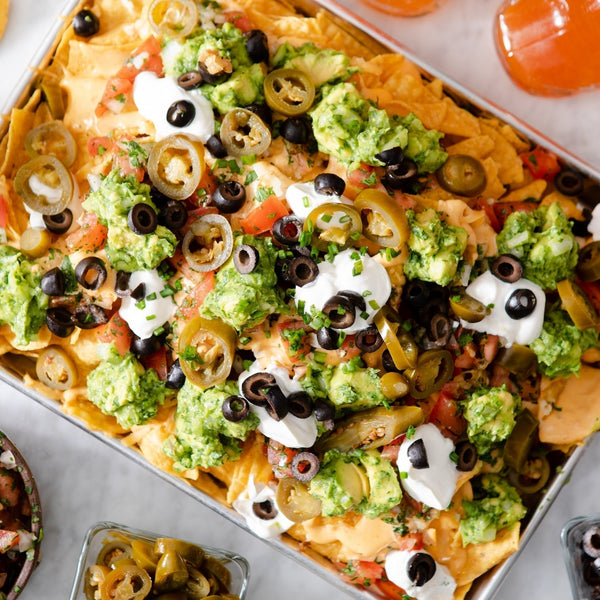A platter of nachos with sour cream, guacamole, black olives, and jalapeños. 