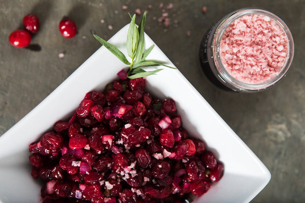 A square bowl of deep red cranberry salsa, next to a jar of pink pinot noir salt.