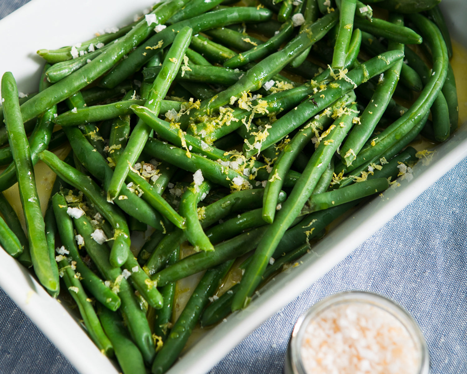 A dish with green beans and a jar of infused lemon zest salt.