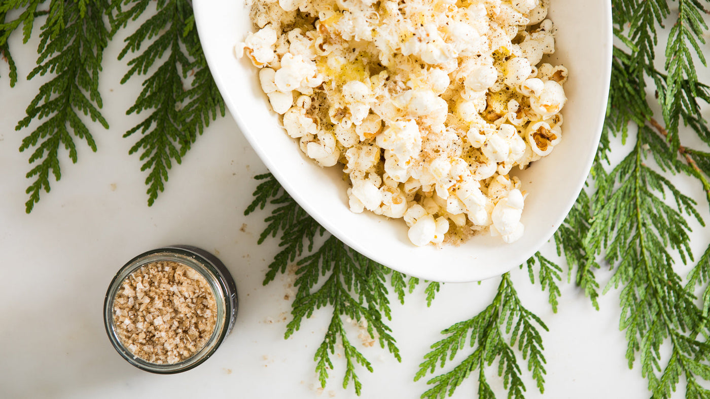 Popcorn in a white bowl sprinkled with truffle salt, next to a jar of truffle salt.