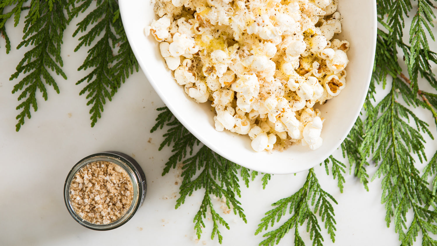 Popcorn in a white bowl sprinkled with truffle salt, next to a jar of truffle salt.