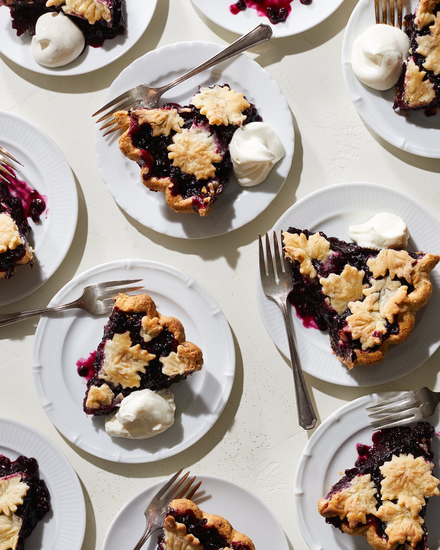 Ten white plates with slices of blueberry pie, dollops of whipped cream, and forks.