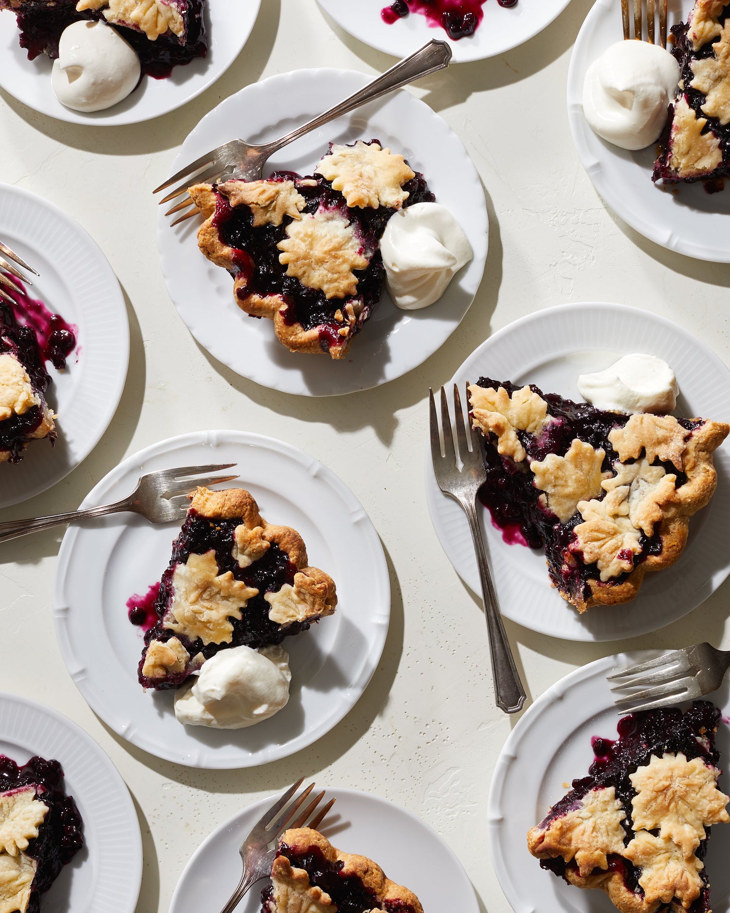 Ten white plates with slices of blueberry pie, dollops of whipped cream, and forks.