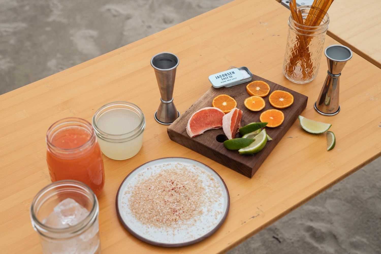 Ingredients to make a grapefruit cocktail, including slices of grapefruit, grapefruit juice, and salt, are laid out on a wooden table