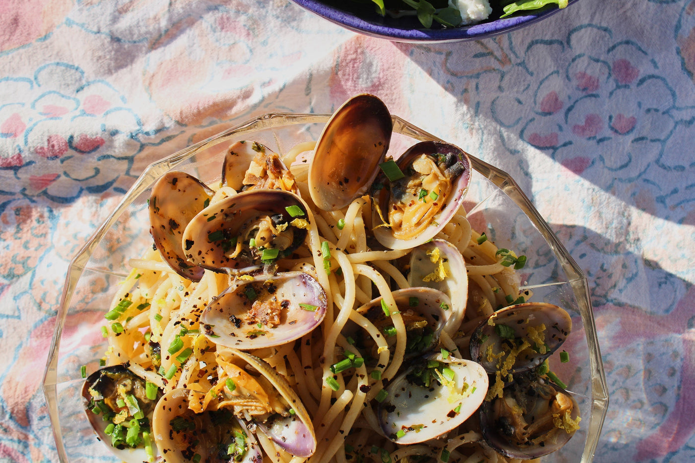 A plate of open clams and pasta noodles sits atop a decorative tablecloth.