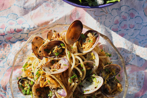 A plate of open clams and pasta noodles sits atop a decorative tablecloth.