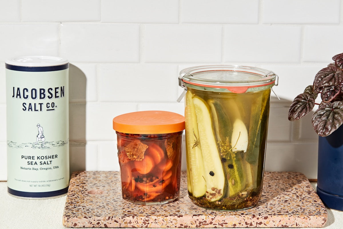 A kitchen counter with a canister of salt and two glass jars of pickled vegetables.