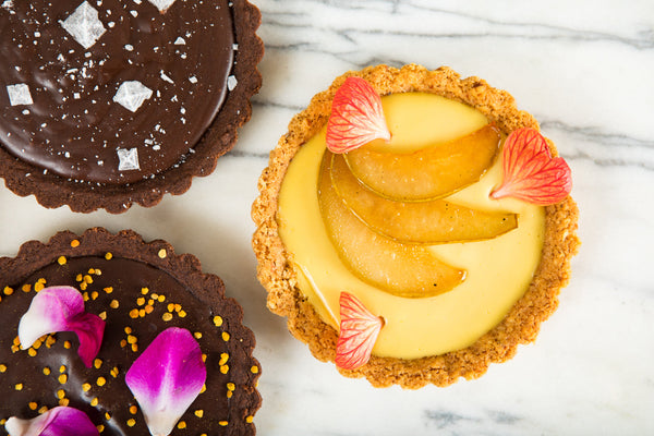 Three custard tarts with various toppings, like salt, fruit, and flower petals.