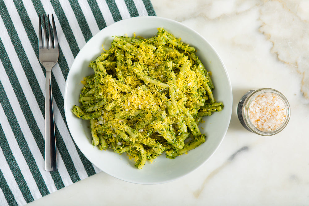 A bowl of green pasta garnished with yellow grated cured egg yolks.