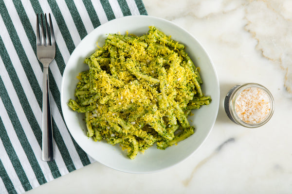 A bowl of green pasta garnished with yellow grated cured egg yolks.