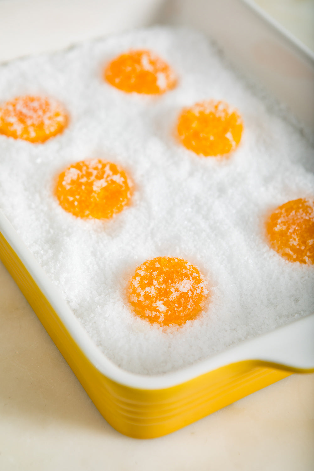Cured egg yolks covered with flaky sea salt in a baking pan.