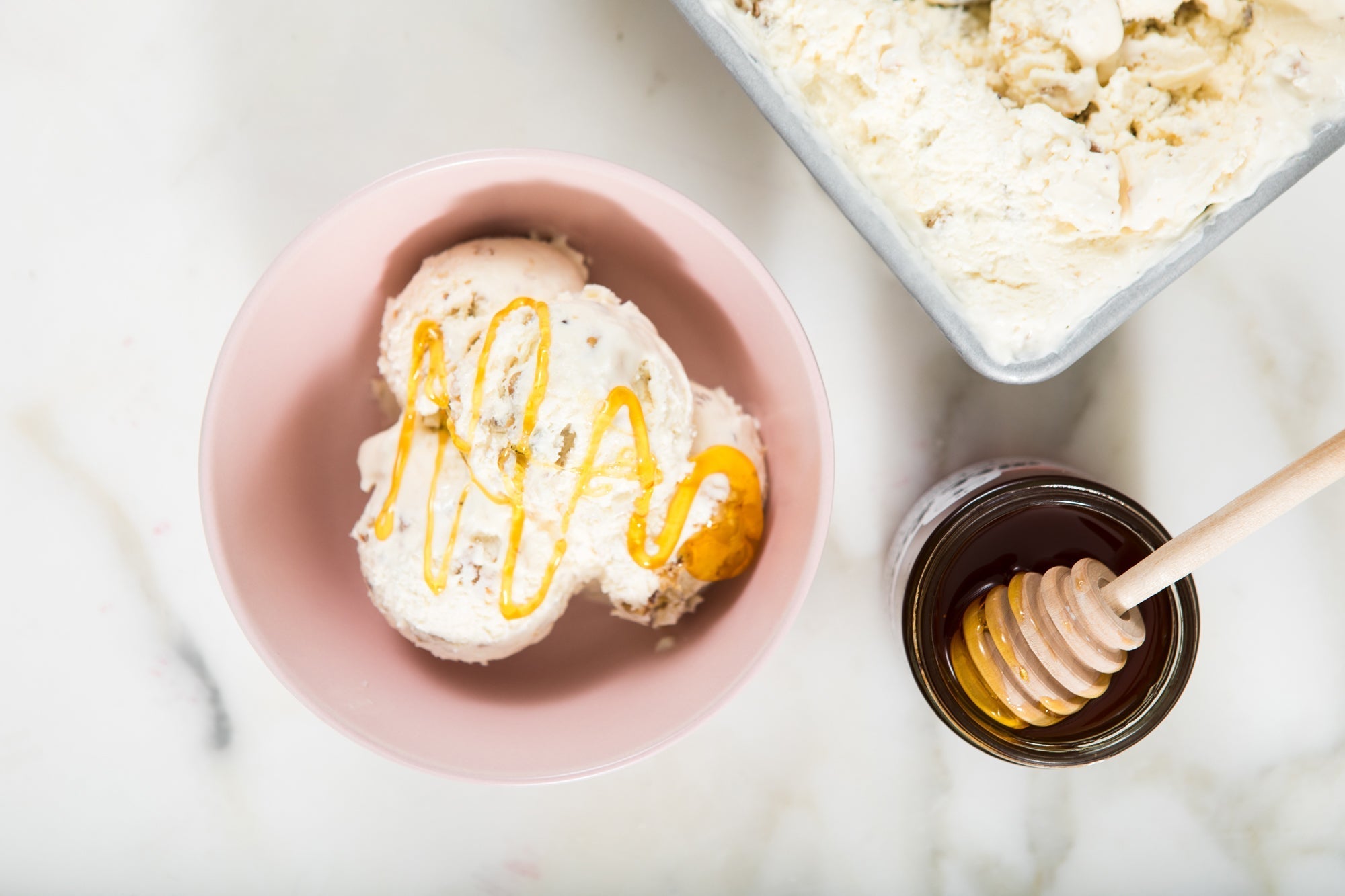 A bowl of ice cream with honey drizzled on top and an open jar of honey with a honey dipper in it.