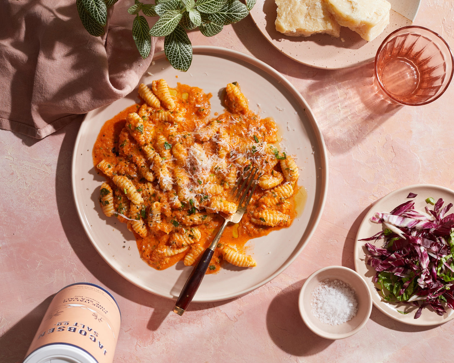 A table scape with bowls of food and a glass of water. In the center is a plate of cavatelli with tomato sauce.
