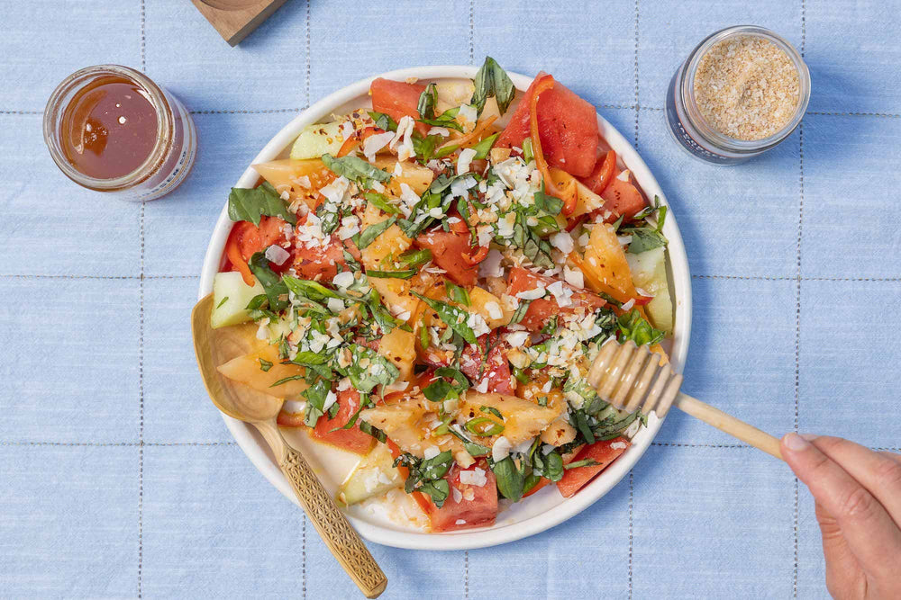 A bowl of salad, a jar of honey, and a jar of salt.
