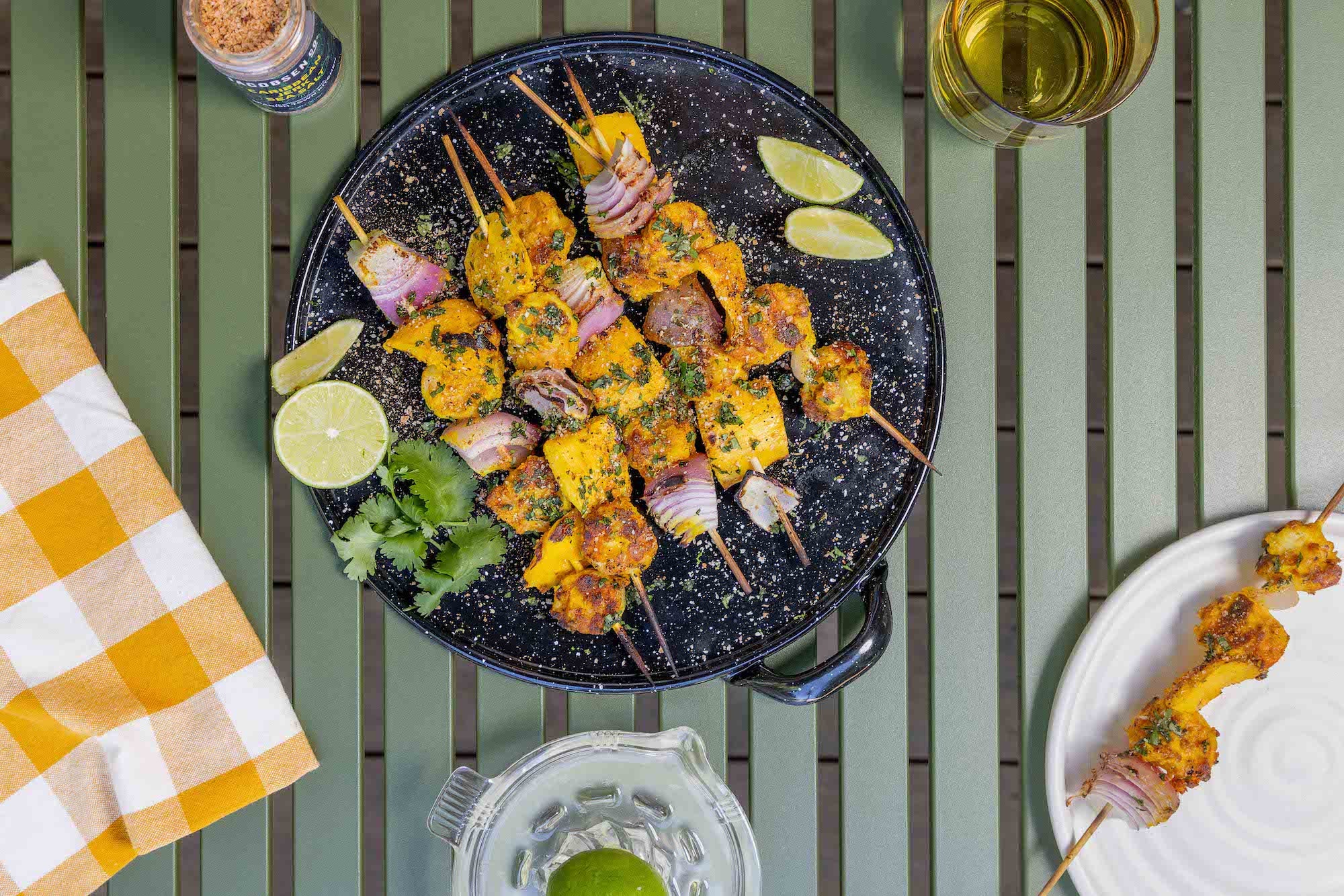 Shrimp and mango skewers, garnished with cilantro and lime, on an enamel dish.