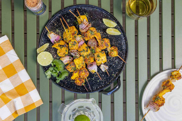 Shrimp and mango skewers, garnished with cilantro and lime, on an enamel dish.