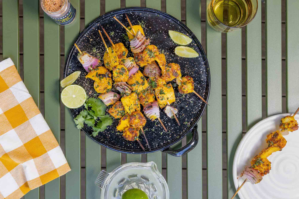 Shrimp and mango skewers, garnished with cilantro and lime, on an enamel dish.