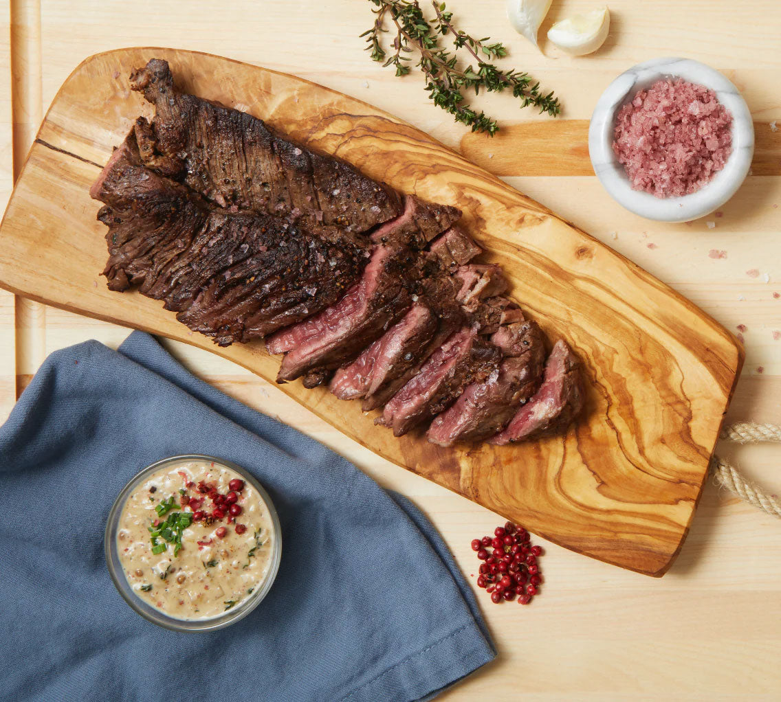 A sliced steak on a cutting board with bowls of Pinot Noir Salt and au poivre sauce. 