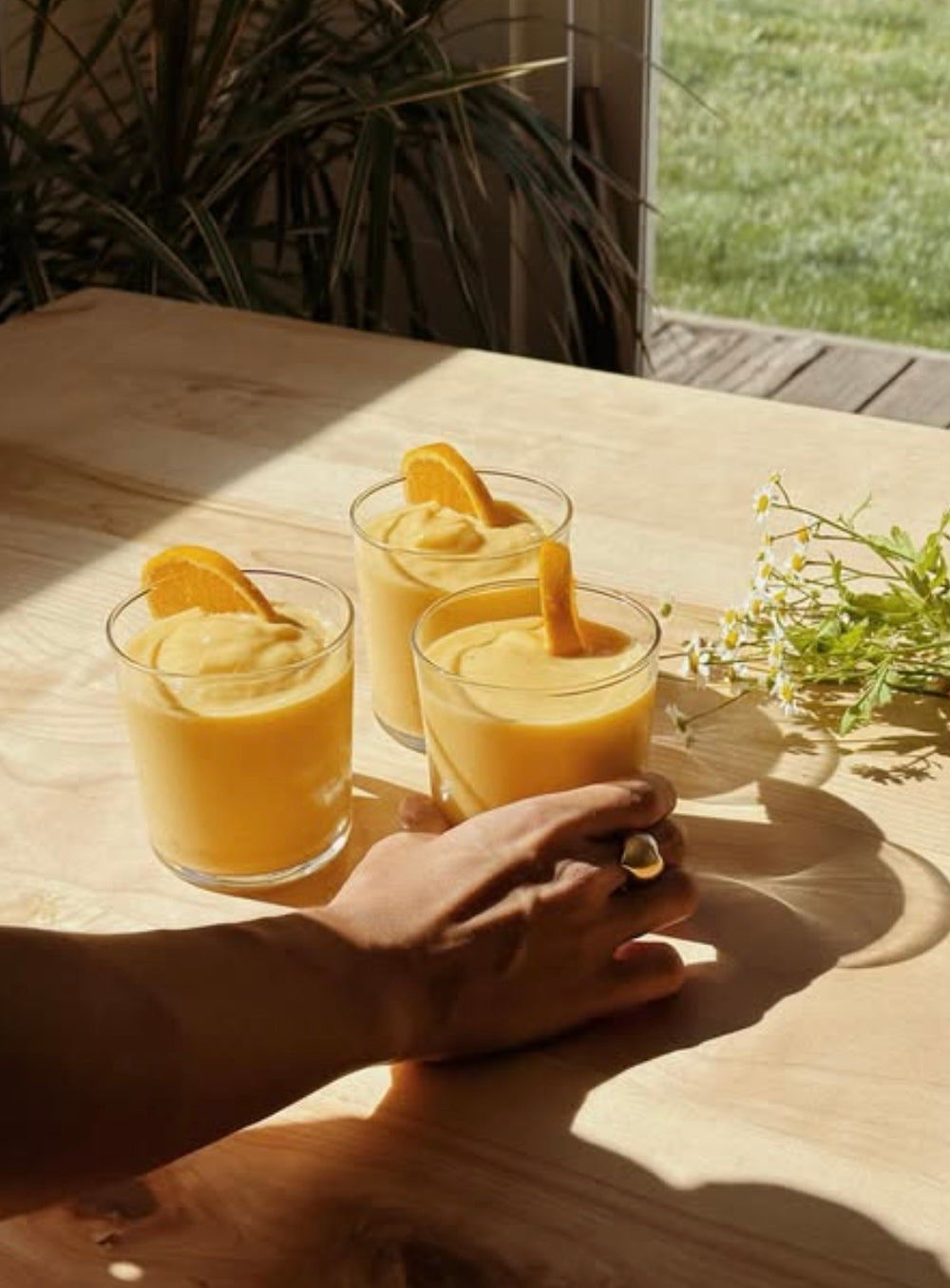 Three cups are filled with orange smoothie. A hand holds the cup on the right.