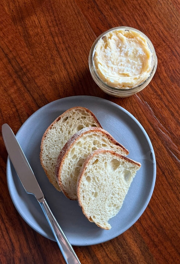 A plate with slices of bread and a butter knife next to a jar of salted butter.