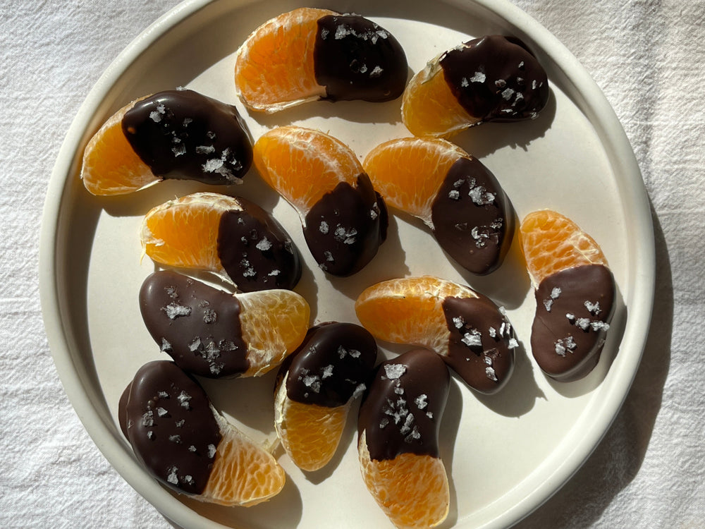 Plate of a dozen orange slices, half dipped in chocolate and sprinkled with flake salt.