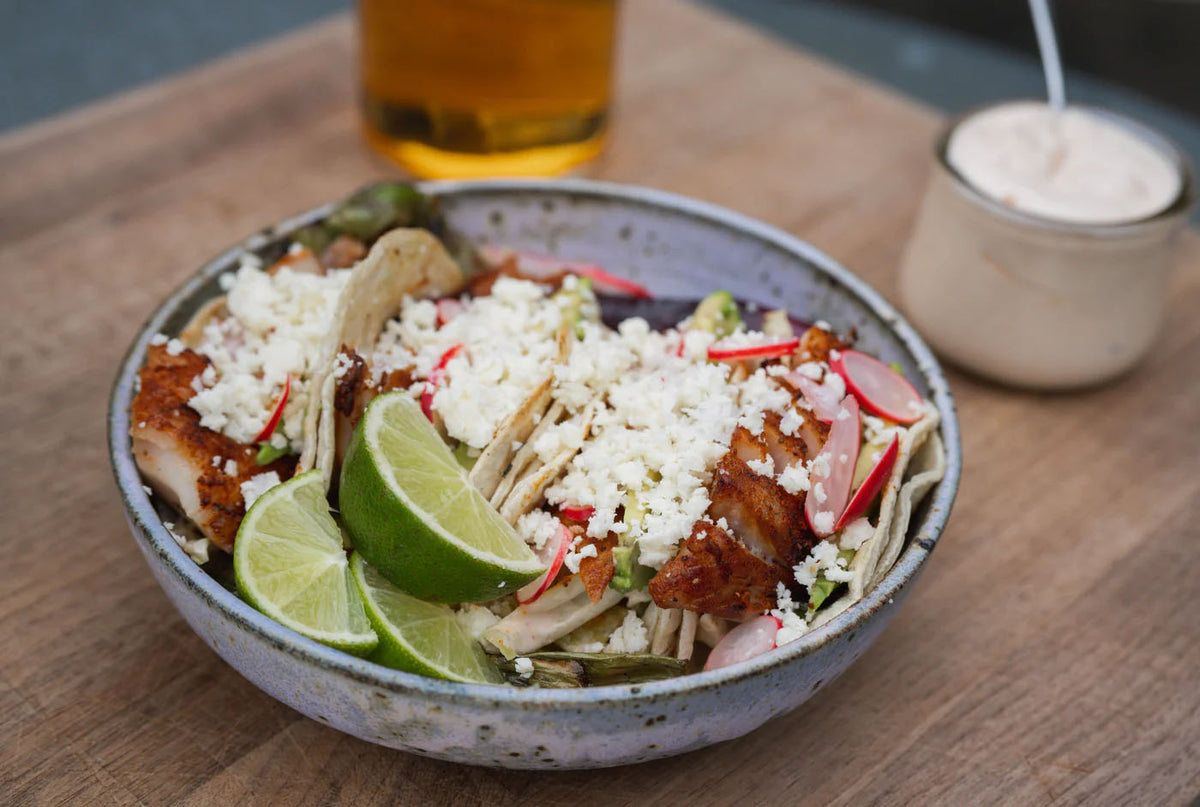 A bowl with grilled fish tacos and limes.