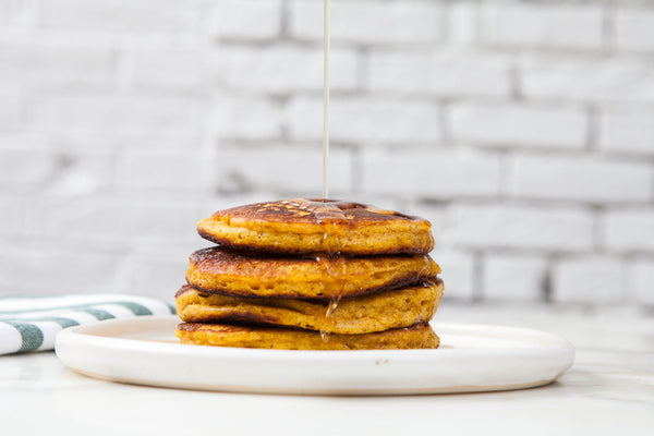 Pumpkin pancakes stacked on a plate, with syrup being poured over. 