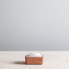 Canyon red salt cellar filled with sea salt on a granite tabletop. 
