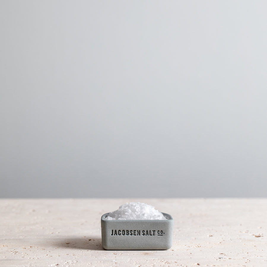 Cool grey colored salt cellar filled with sea salt on a granite tabletop. 