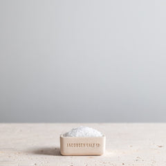 White salt cellar filled with sea salt on a granite tabletop. 