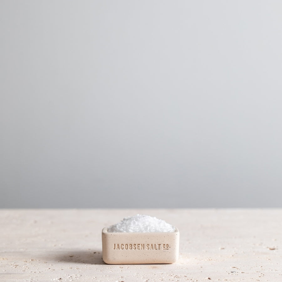 White salt cellar filled with sea salt on a granite tabletop. 