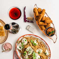 A table scape featuring jalapeno poppers, pasta, wine, pinot noir salt and a slide tin of infused black pepper salt. 