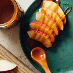 Caramel sauce drizzled over sliced apples on top of a green plate.