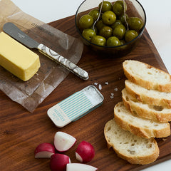 Small sea salt slide tin on a cutting board with sliced bread, butter, olives and radishes. 
