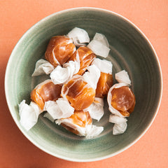 Wrapped hazelnut caramels in a green bowl on an orange backdrop.