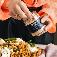 Jacobsen Infused Garlic Salt, held by a woman with hands reaching into the jar in preparation to sprinkle salt onto pasta.