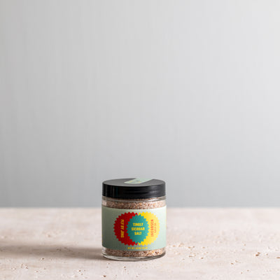 A jar of JSC x FBJ Tingly Sichuan Salt with colorful label on blue backdrop