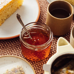 A Jar of Jacobsen Honey on a table scape with plates of cornbread and cups of coffee.