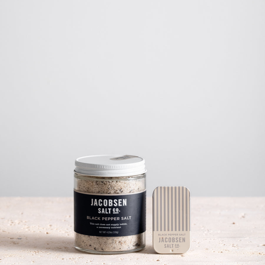 A jar of Jacobsen Infused Black Pepper Salt next to a matching slide tin of the same product. 